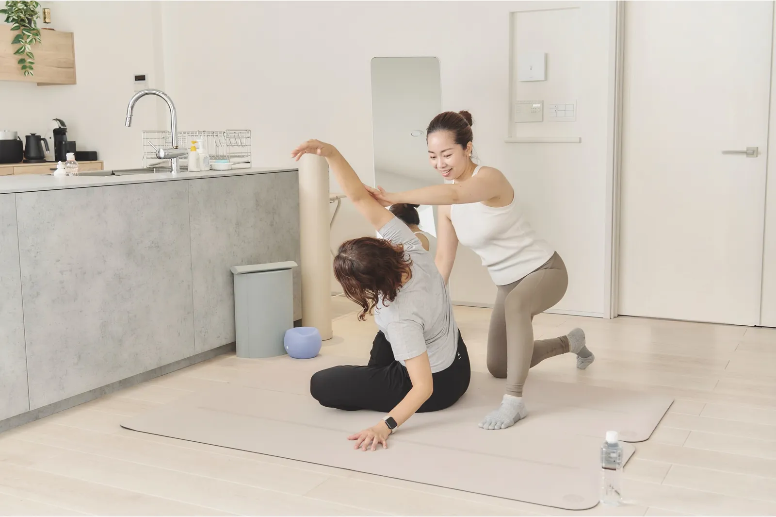 キッチン横にマットを敷いて、自宅でストレッチを手伝うトレーナー