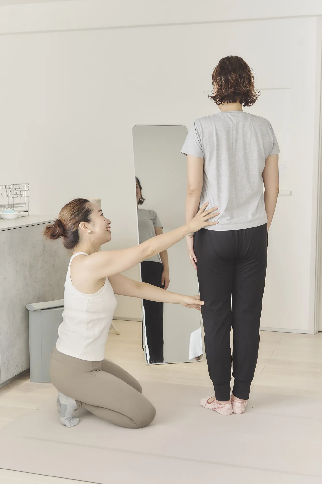 鏡の前に立つお客様の背中と腰に手を添えて、立ち方を一緒に確かめるトレーナー