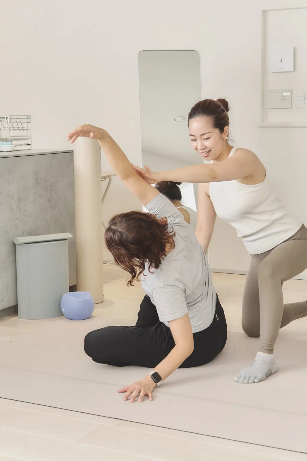 女性専用の出張パーソナルトレーニングで、自宅のマットでストレッチを手伝うトレーナー