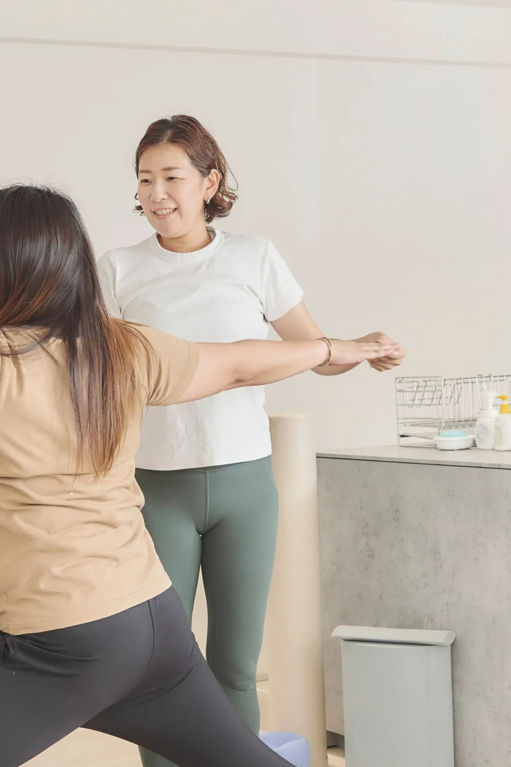 腕を前に伸ばすお客様の手を、横から支えるトレーナー