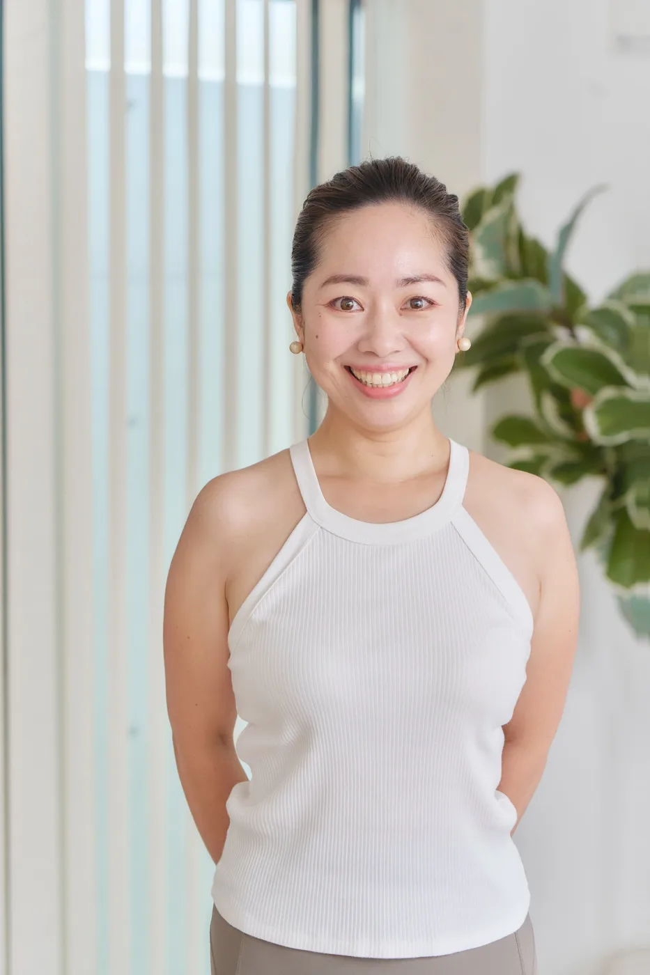 髪をまとめ、白いタンクトップ姿で手を後ろに組むトレーナー
