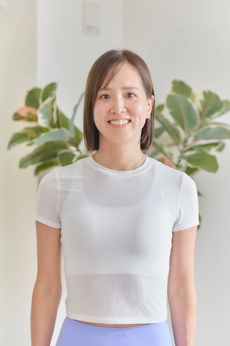 肩にかかるボブの髪で、白いTシャツを着て微笑むトレーナー