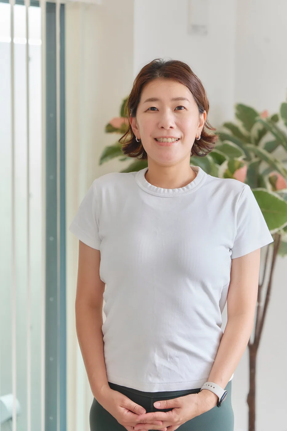 肩までの髪で、白いTシャツを着て手を前で組むトレーナー