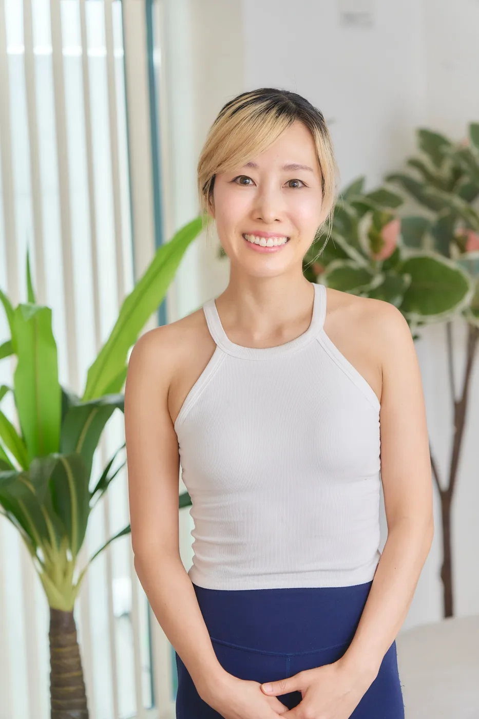明るい髪をまとめ、白いタンクトップ姿で微笑むトレーナー